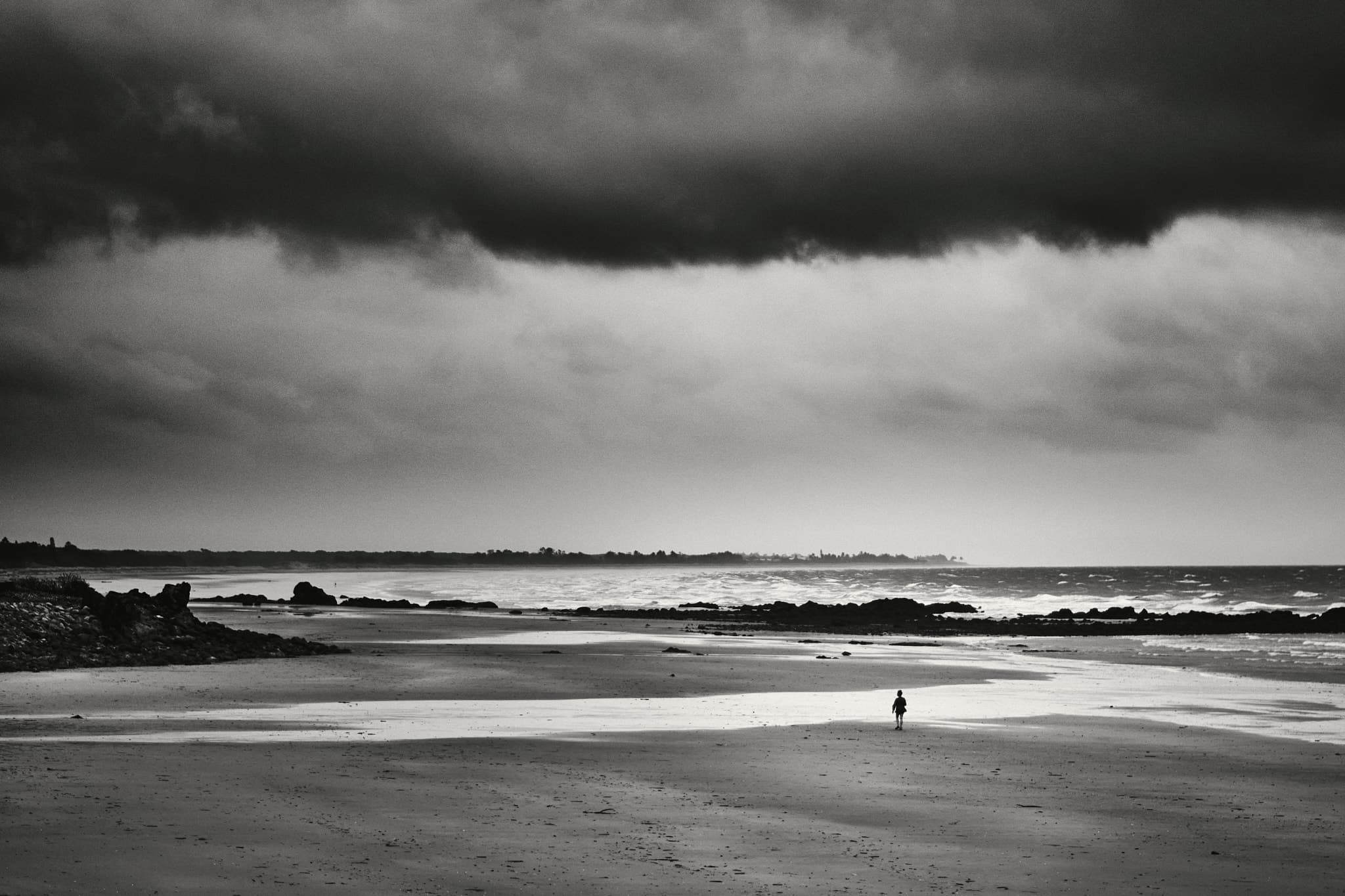 Lone figure on beach under stormy sky, Yeppoon