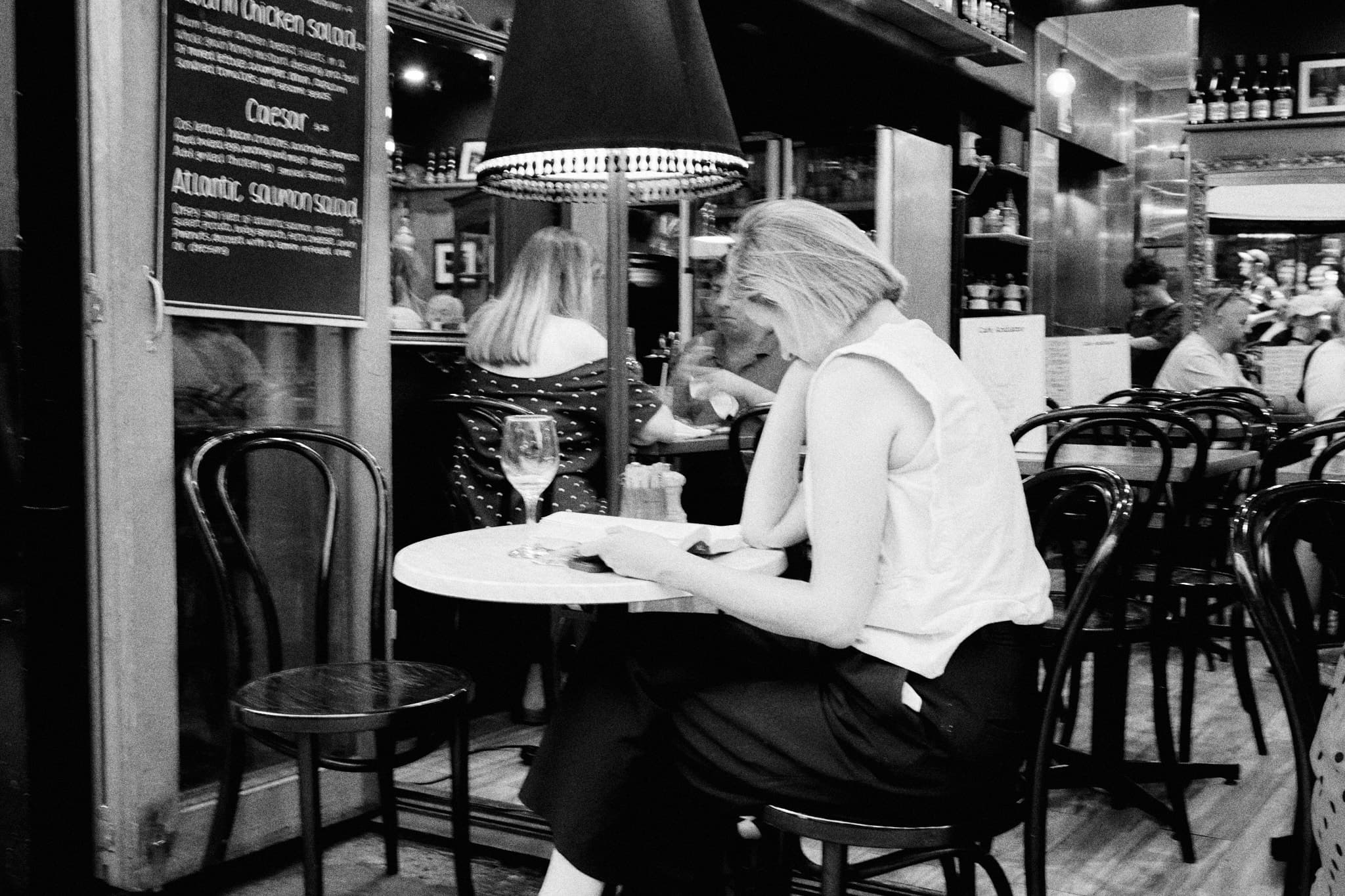 Woman alone at cafe with wine and book, surrounded by people